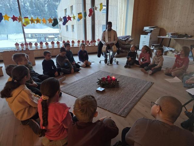 Pfarrer mit Kinder vor dem Adventkranz