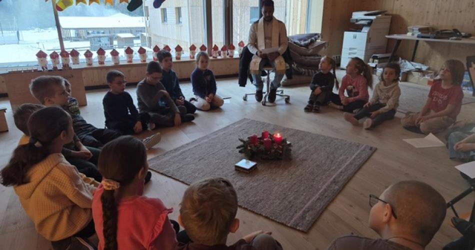 Pfarrer mit Kinder vor dem Adventkranz